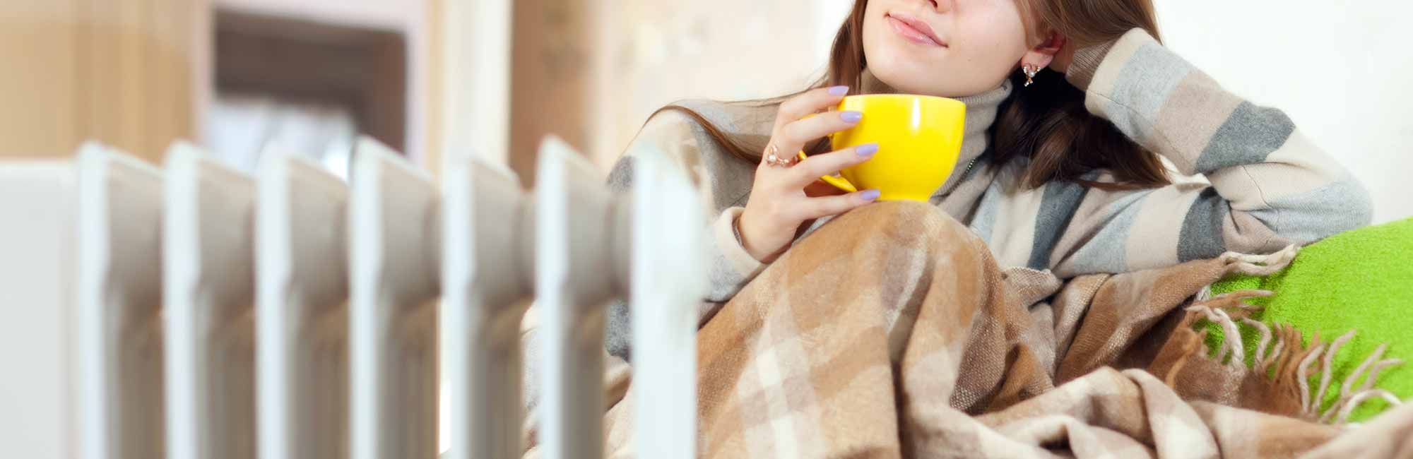 Woman holding a cup and sitting in front of a heater.